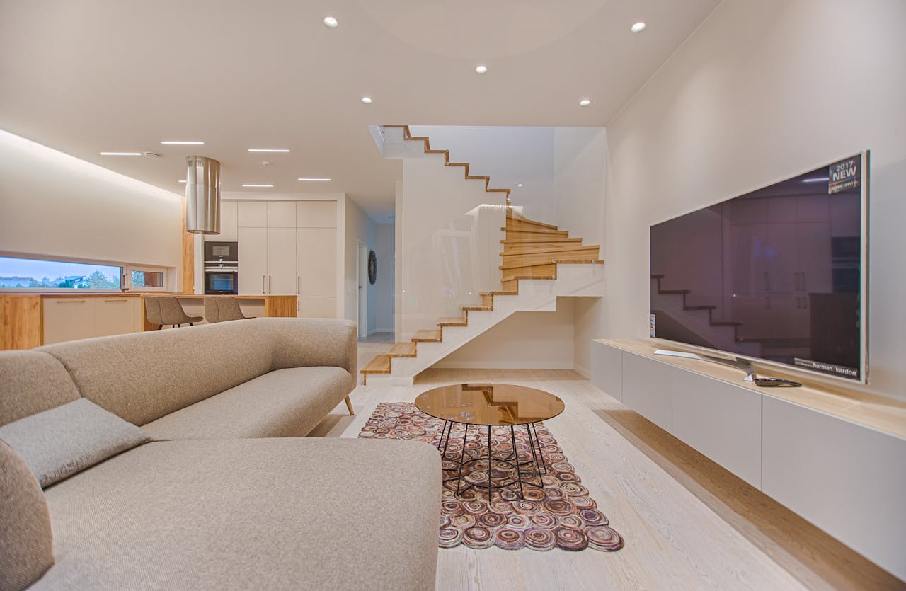 about-us Spacious modern living room featuring stairs, a TV, and sleek furniture design.